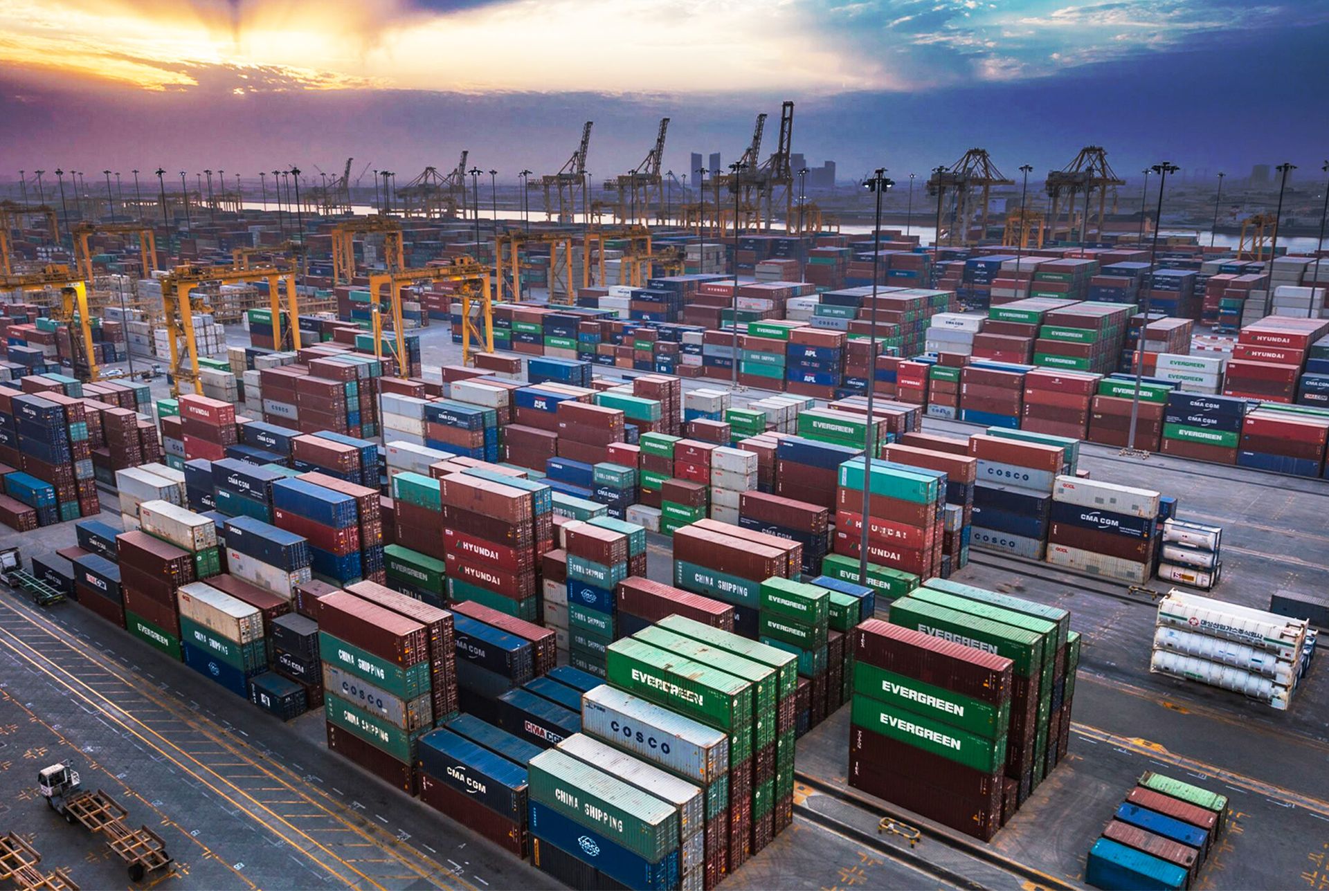 Container terminal with cranes and stacked shipping containers at dusk